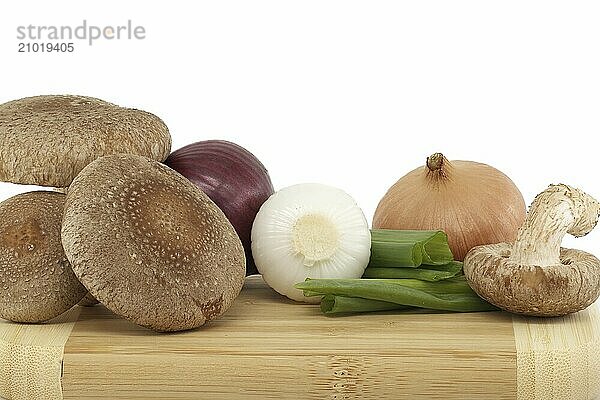 Shiitake mushrooms and various onions on a wooden cutting board isolated on white background. Recipes and medicinal herbs