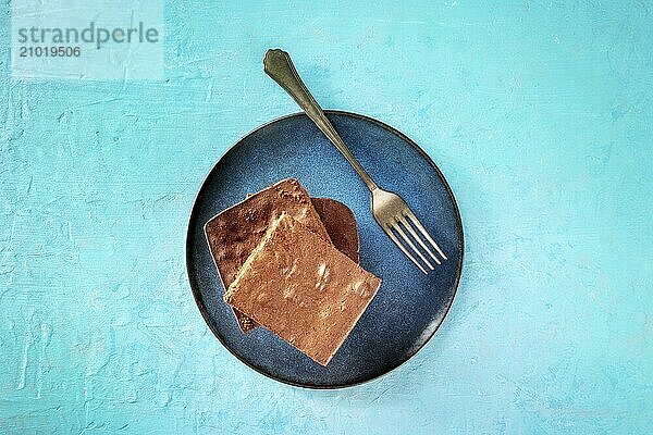 Chocolate brownie  simple coffee cake  overhead flat lay shot on a vibrant blue background  on a plate with a fork