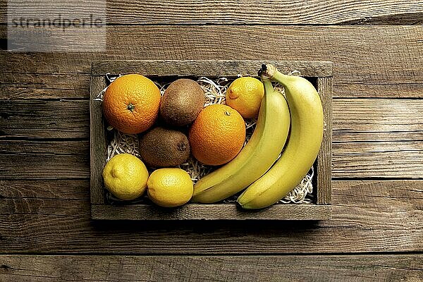 Fresh tropical fruits in a wooden delivery box on a wooden background. Orange  banana  kiwi and lemon top view flat lay with copy space for some advertisement text