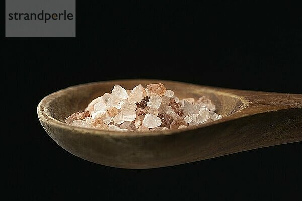 A close up photo of coarse himalayan sea salt on a wooden spoon against a black background