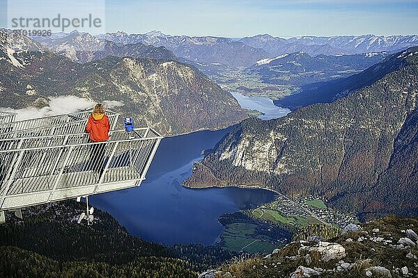 A hiker stands on the 5fingers viewpoint. View from the Dachstein Krippenstein to Lake Hallstatt. Hallstatt on the left  Obertraun on the right. Autumn  good weather. Some clouds in the mountains. Lake Hallstatt  Salzkammergut  Upper Austria  Austria  Europe