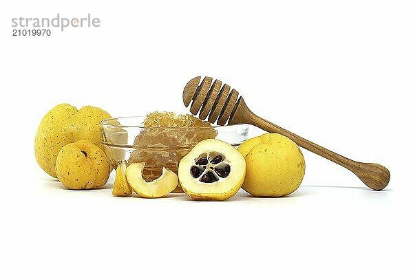 Glass bowl brimming with honey and wooden dipper resting on its rim surrounded by vibrant quince fruits  both sliced and whole isolated on white background  full depth of field