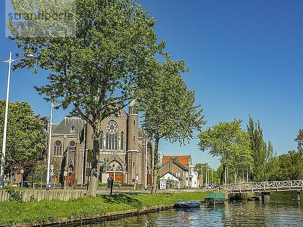 Church with imposing architecture  trees and small canal with boats and bridge  alkmaar  the netherlands