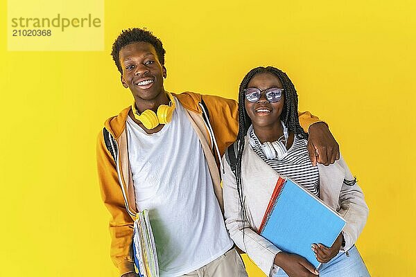 Studio portrait with yellow background of two male and female university african colleagues embracing and smiling at camera