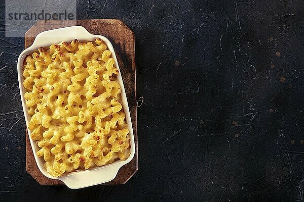 Macaroni and cheese pasta in a casserole dish  shot from the top on a black background with a place for text  Food photography