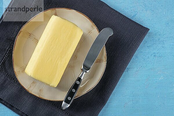 A block of butter with a knife on a plate  overhead flat lay shot on a vibrant blue background  with copy space  Food photography