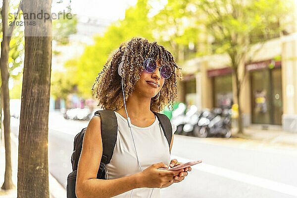 Side view close-up with copy space portrait of a latin cheerful woman listening to music using phone in the street