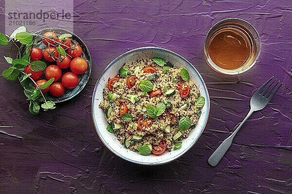 Quinoa tabbouleh salad in a bowl  a healthy dinner with tomatoes and mint  overhead flat lay shot with a drink on a purple background  Food photography  Food photography