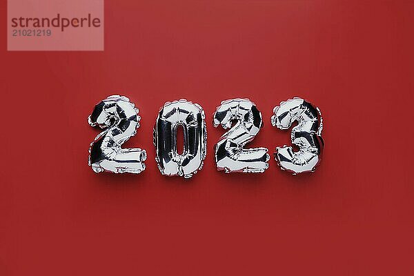 Christmas or New Year background. Red color flat lay with silver shiny 2023 balloon numbers in the center. Simple minimalistic greeting card