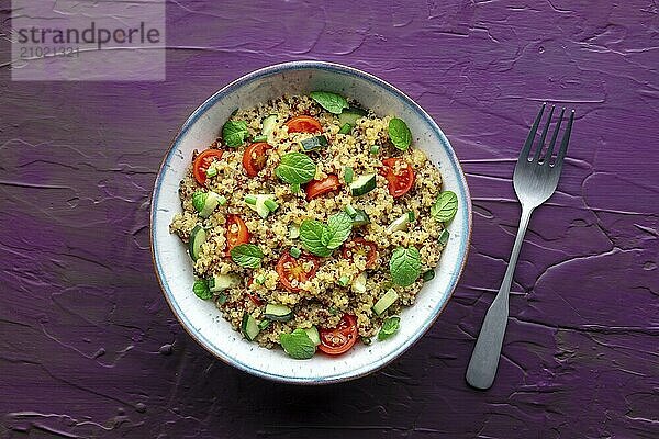 Quinoa tabbouleh salad in a bowl  a healthy dinner with tomatoes and mint  overhead shot with a fork on a purple background  Food photography