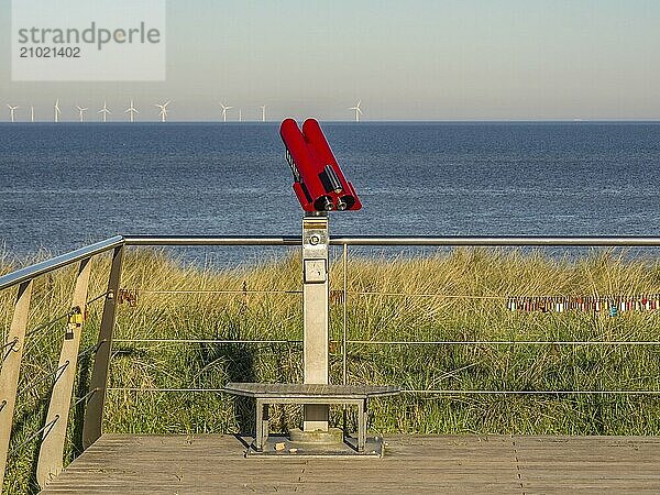 A red telescope on a wooden platform with a view of the sea and wind turbines in the background  egmond aan zee  the netherlands