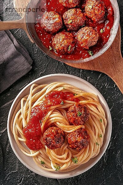 Meatballs. Beef meat balls  overhead flat lay shot in a pan and with a plate of spaghetti pasta  on a black background  Italian cuisine  Food photography