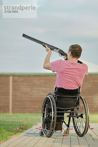 Rear view of a man in a wheelchair aiming at a clay pigeon at outdoor shooting range