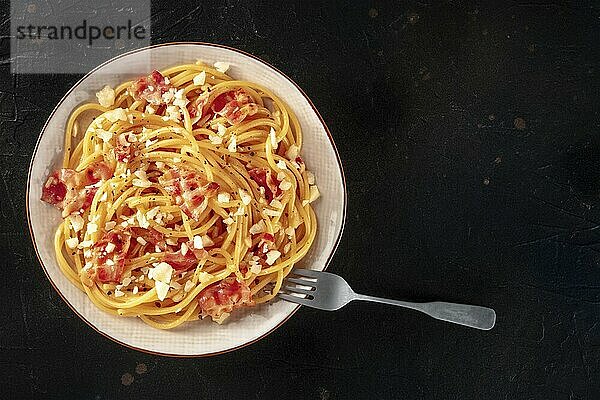 Carbonara pasta dish  traditional Italian spaghetti with pancetta and cheese  overhead flat lay shot with a fork and copy space  on a dark background  Food photography