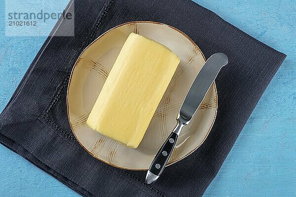 A block of butter with a knife on a plate  overhead flat lay shot on a vibrant blue background  Food photography