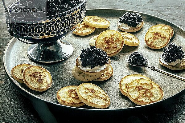 Blinis with black caviar and cream cheese  on a festive dish on a black background  mini pancakes  an elegant appetizer  Food photography  Food photography