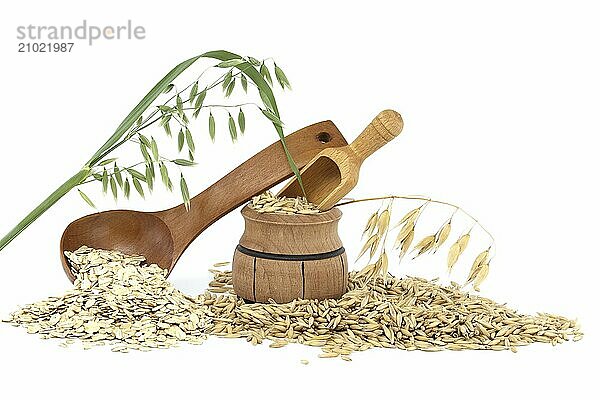 Oat groats rolled and flattened into flakes in wooden spoon and oat grains with hulls or husks spilling from a wooden barrel isolated on white background