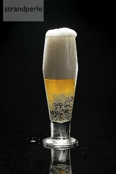 A close up uof a glass of beer against a black background starting to overflow