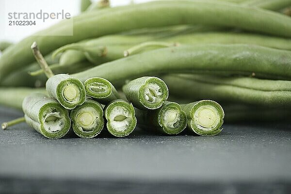 Heap of cut green beans on black stone table over white background. Organic and diet food