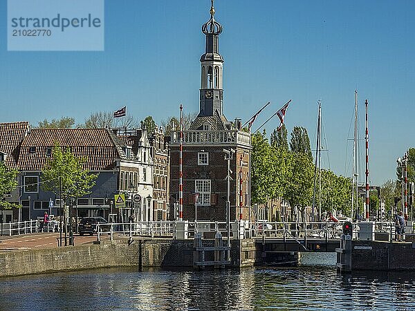 Historic tower on a canal with trees and houses in the background in sunny weather  alkmaar  the netherlands