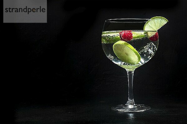 Fancy cocktail with fresh fruit. Gin and tonic drink with ice at a party  on a black background. Alcohol with lime and raspberry  with a place for text