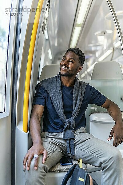 Vertical photo of a happy african entrepreneur sitting on the metro looking through window