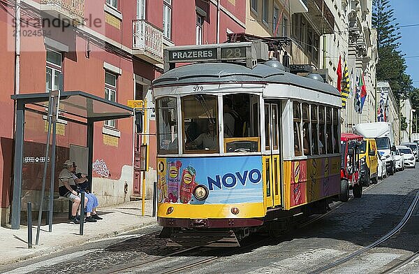 A yellow-purple tram with Novo advertising runs along the street with people in the background  Tram  Line 28  Carros eléctricos de Lisboa  Eléctricos de Lisboa  Old Town  Lisbon  Portugal  Europe