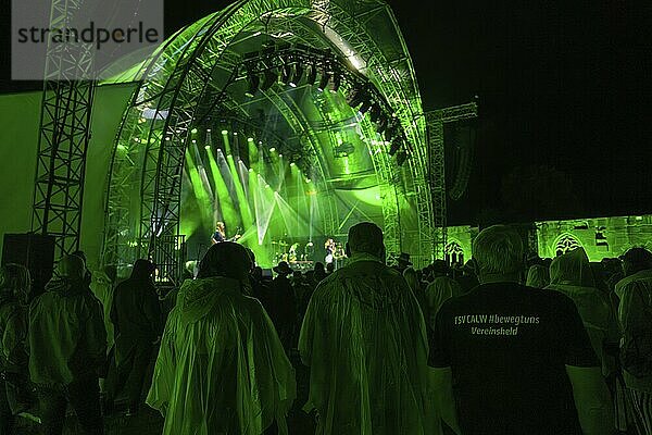 People in rain ponchos and a T-shirt in the crowd at a night concert with green stage lighting  Klostersommer  Calw Hirsau  Black Forest  Germany  Europe