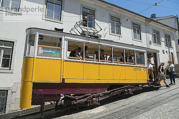 Yellow tram stops at a stop as passengers get on and off in a sunny city  funicular railway  Ascensor da Glória  Old Town  Lisbon  Lisboa  Portugal  Europe