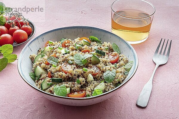 Quinoa tabbouleh salad in a bowl  a healthy dinner with tomatoes and mint  with a fork and a drink on a pink background