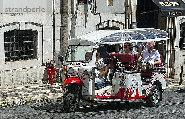 White and red tuk-tuk with tourists on a city street in summer conditions  historic centre  Lisbon  Lisboa  Portugal  Europe