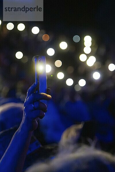 Close-up of a hand holding an illuminated smartphone in a crowd at night  focus on the light  Klostersommer  Calw Hirsau  Black Forest  Germany  Europe