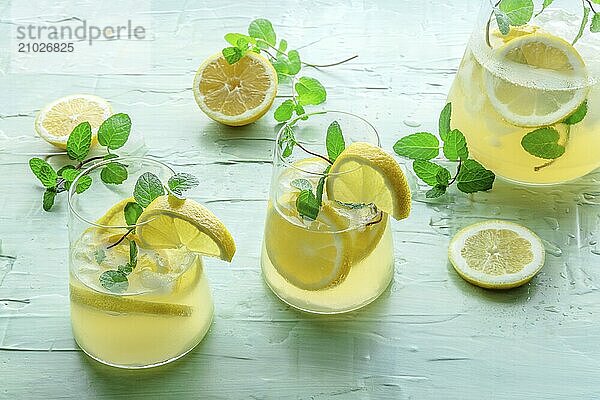 Lemonade with mint. Lemon water drink with ice. Two glasses  a pitcher and lemons on a blue background. Detox beverage. Fresh homemade cocktail