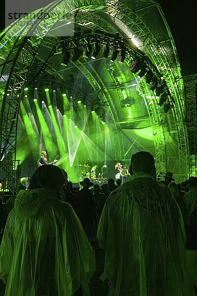 Audience in rain ponchos at a night concert in front of a green-lit stage  Klostersommer  Calw Hirsau  Black Forest  Germany  Europe