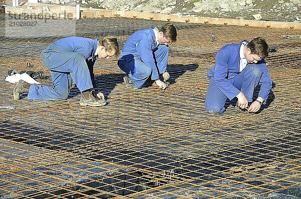 Builders tie off sections of reinforcing for concrete slab foundation of a large building