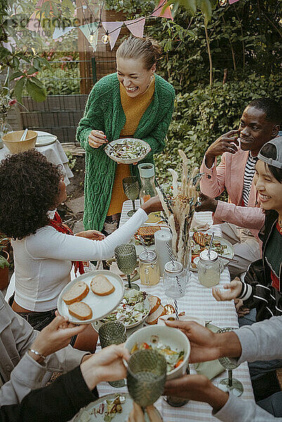 High angle view of happy male and female friends enjoying food and drinks at dining table in dinner party