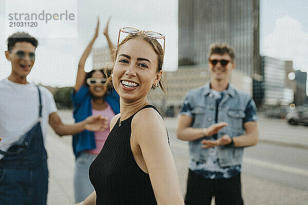 Portrait of happy young woman with friends spending leisure time on street in city