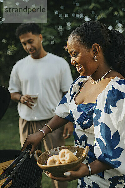 Happy woman barbecuing corn with male family member during garden party