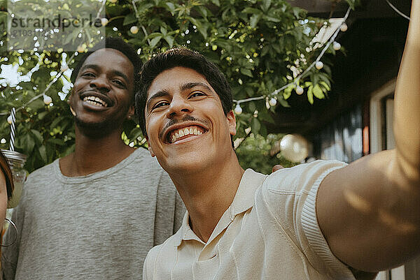 Smiling young man taking selfie with male friend at dinner party