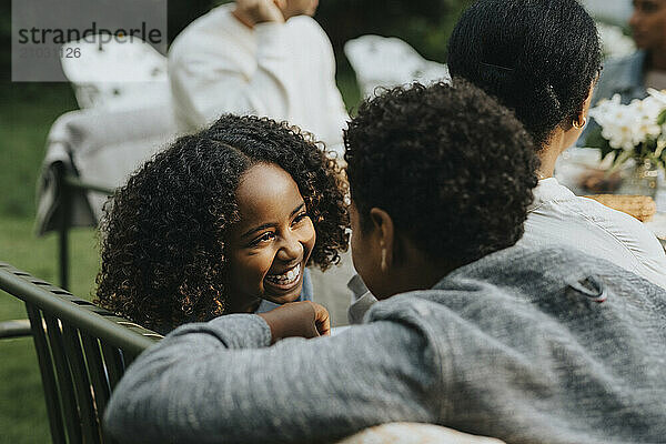 Happy girl talking with male friend during dinner party in garden