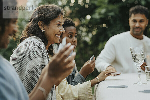 Male and female family members playing cards during social gathering at garden party