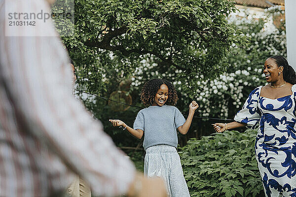 Cheerful girl dancing with family members at garden party in back yard