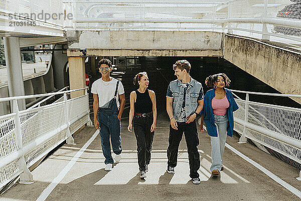 Happy fashionable male and female friends walking on footpath of parking garage at sunny day