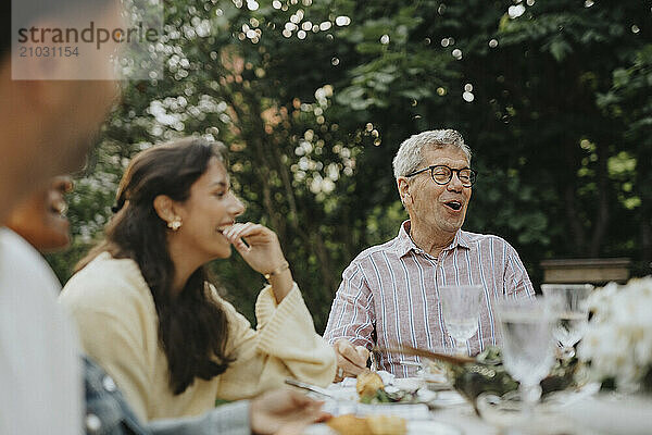 Cheerful senior man enjoying and having fun with family members at lunch party