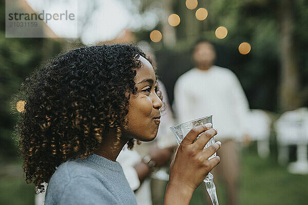 Side view of curly hair girl drinking water in back yard