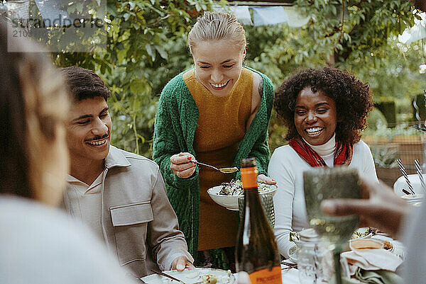 Smiling woman serving salad to male and female friends at dinner party in back yard