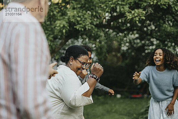 Active senior woman dancing with family members during social gathering at garden party