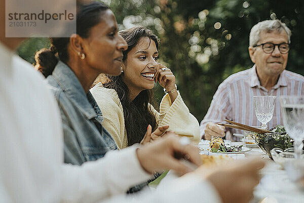 Happy teenage girl having lunch with family members during social gathering