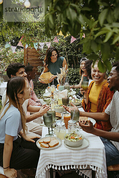 Cheerful male and female friends enjoying food and drinks at dining table