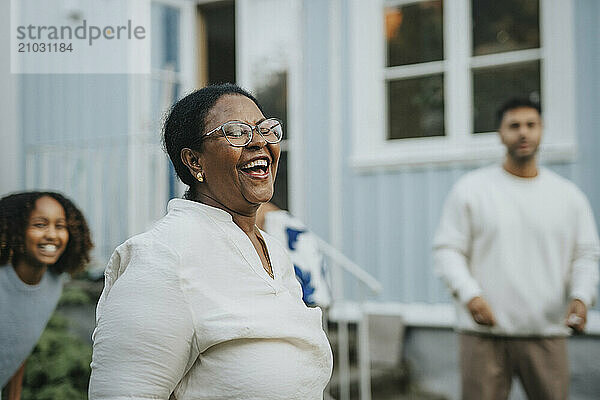 Carefree senior woman dancing and enjoying with family members in back yard